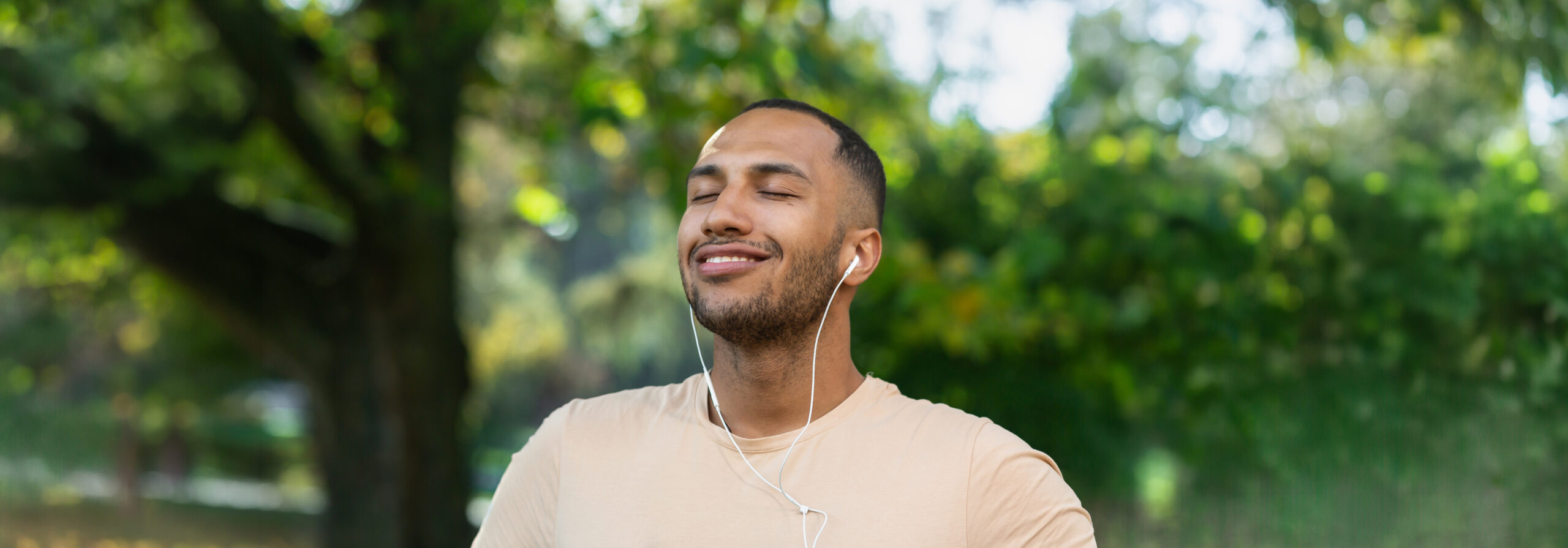 Close-Up Portrait of Man in Park Wearing Headphones Listening to Music Outdoors and Smiling