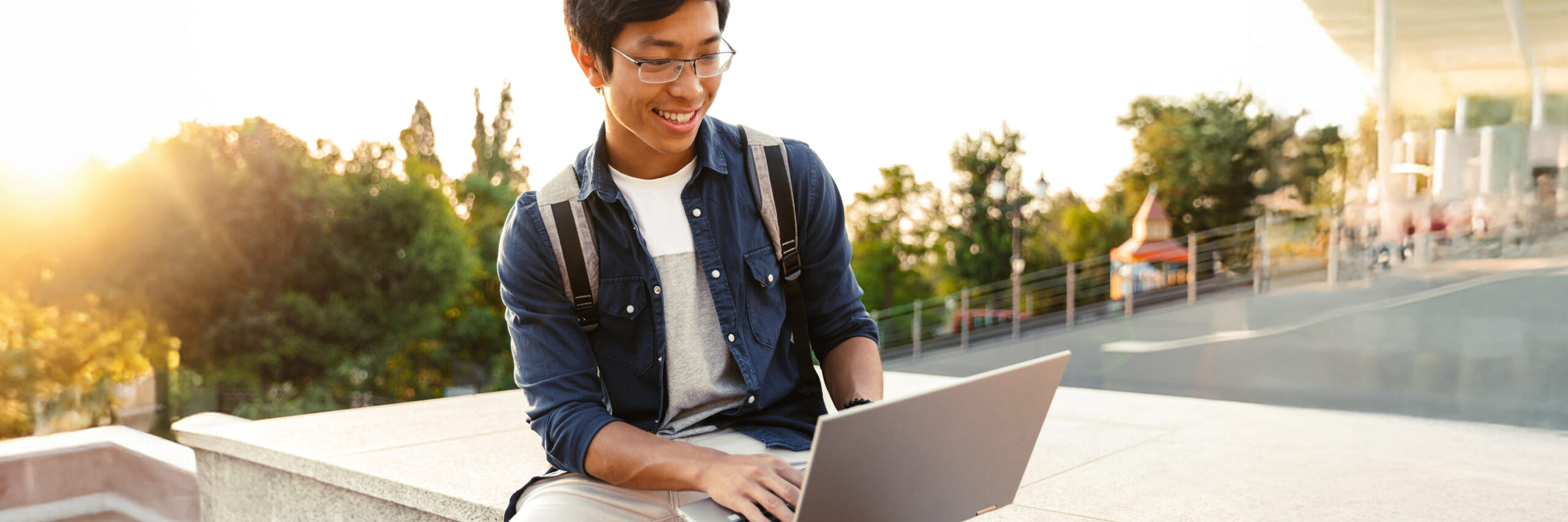 A person sitting outdoors with a laptop on their lap in a public space.