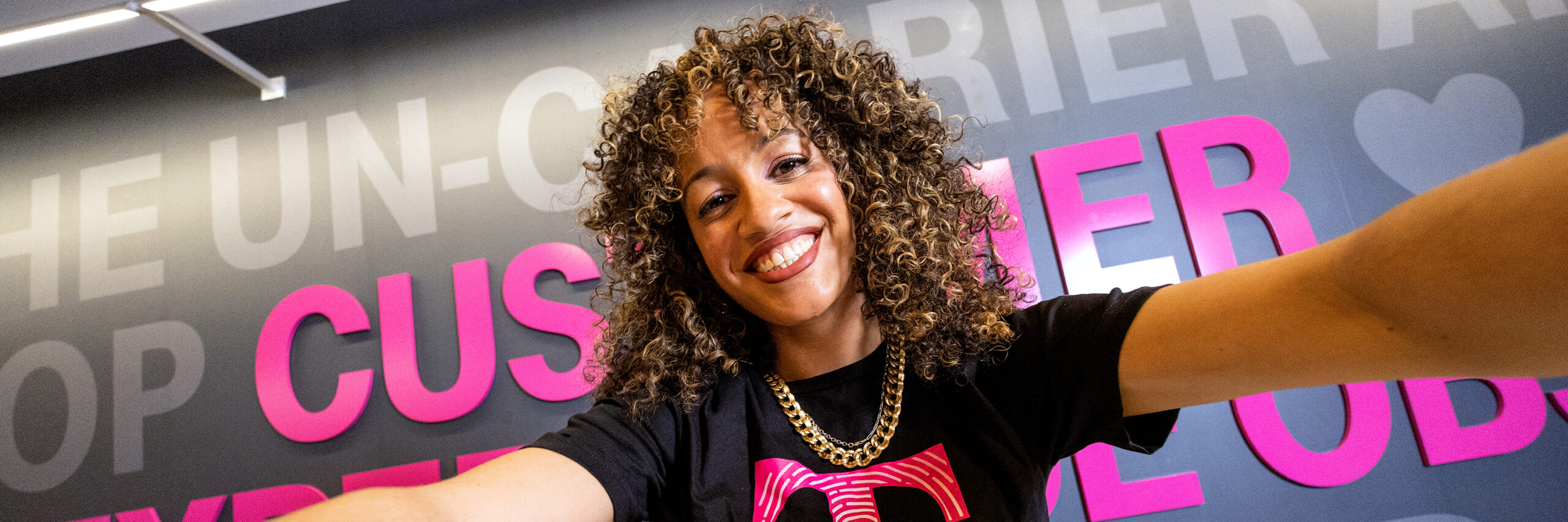 A T-Mobile employee taking a selfie in front of a gray T-Mobile decorated wall.
