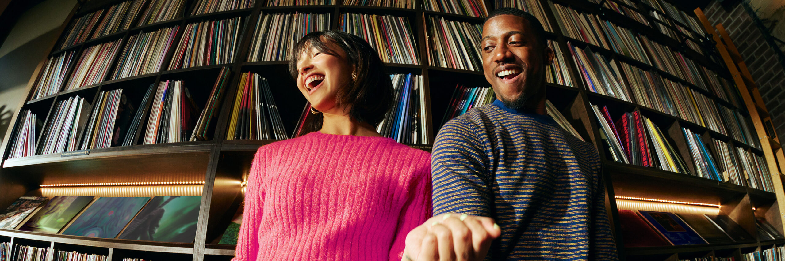 Two people standing in front of shelves filled with books and vinyl records.