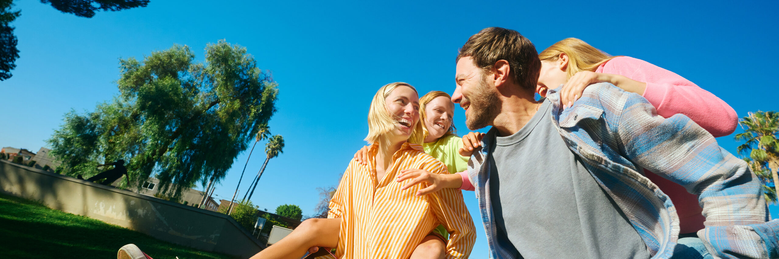 A family outdoors in a park with trees and blue sky.