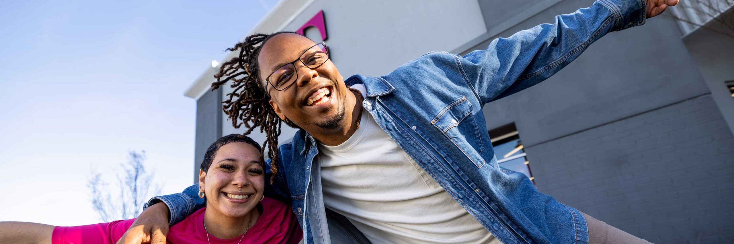 Two T-Mobile employees smiling and laughing together in front of a T-Mobile office building.
