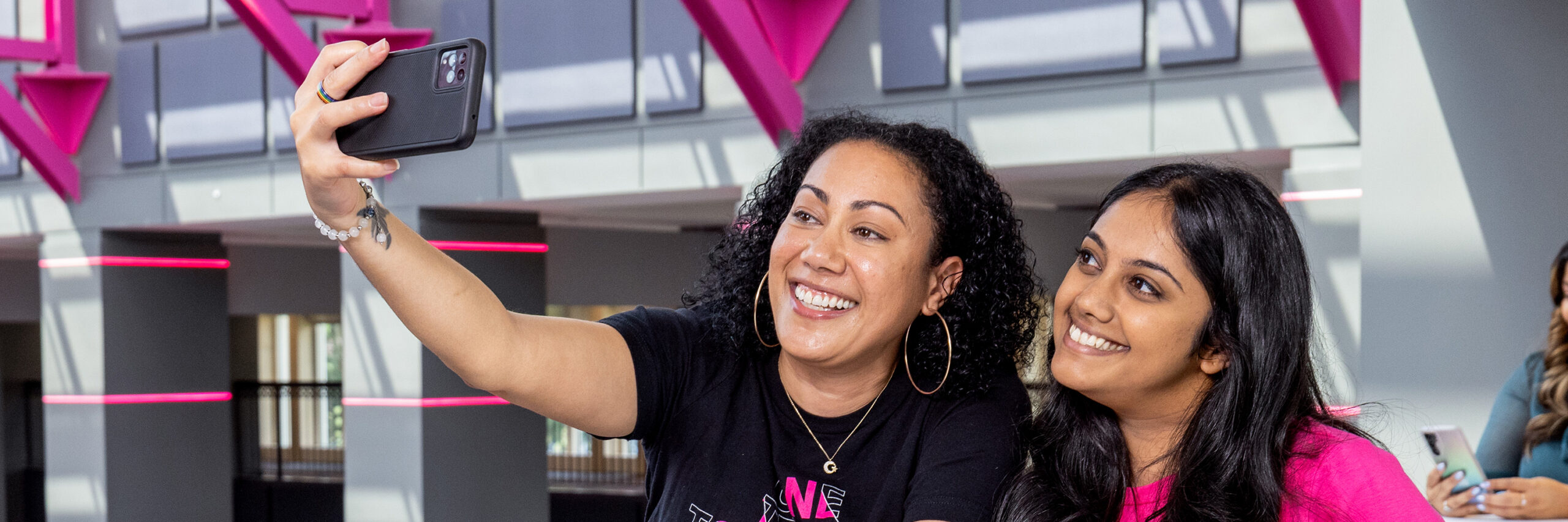 Two T-Mobile employees taking a selfie in front of a pink-accented building.