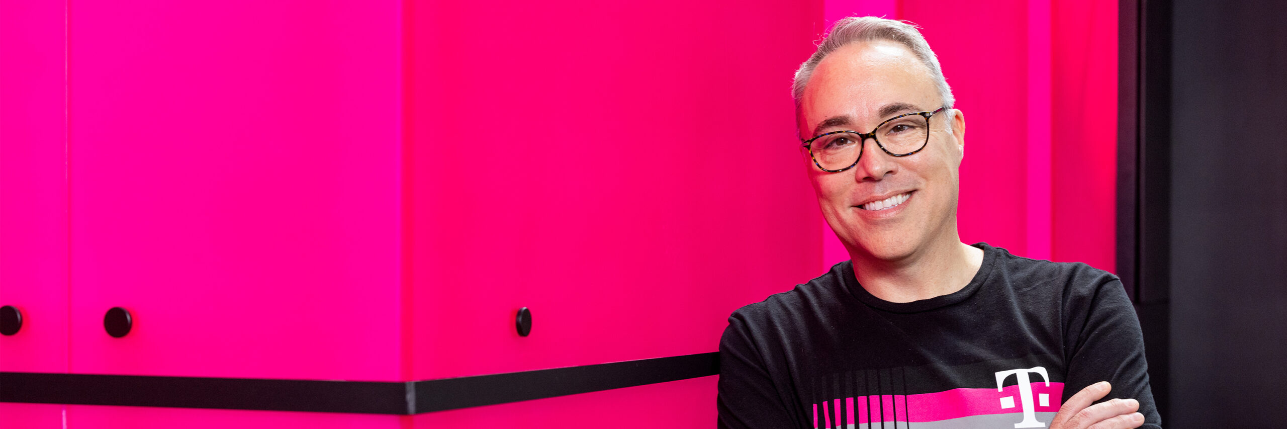 A T-Mobile employee in T-Mobile shirt standing in front of bright pink background.