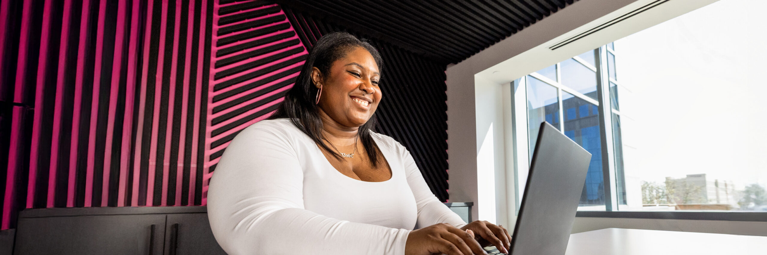 A T-Mobile employee typing on a laptop in a room with a pink and black striped wall.