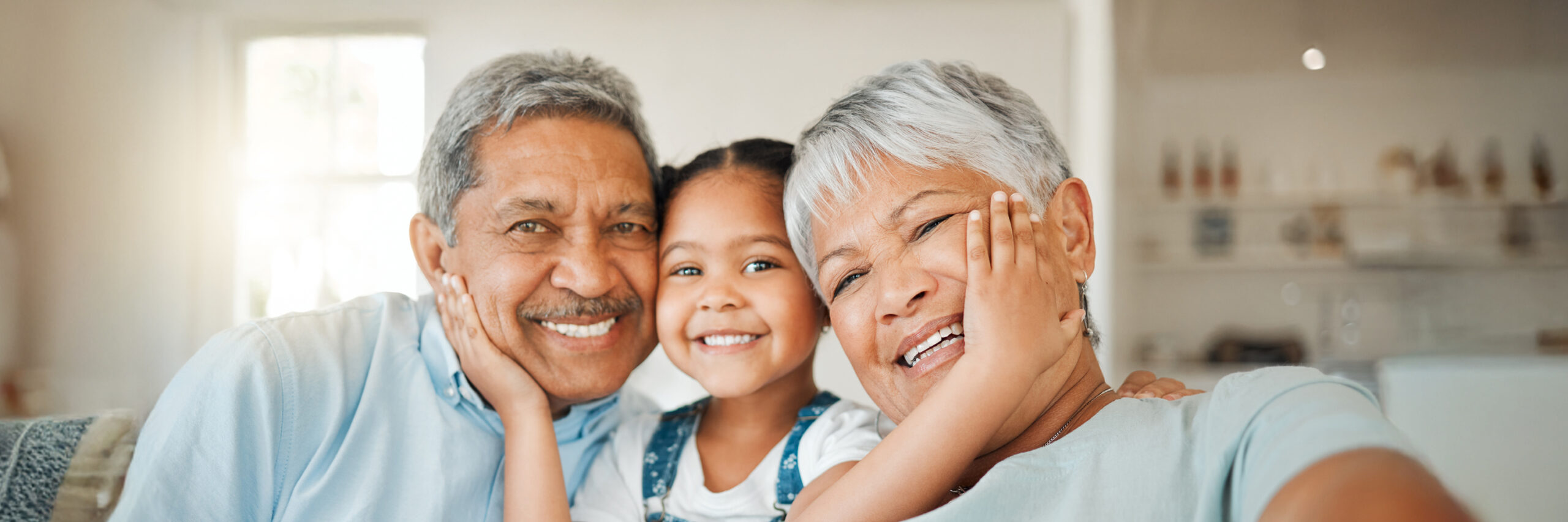 Two grandparents and their granddaughter sitting together in a sunlit room.