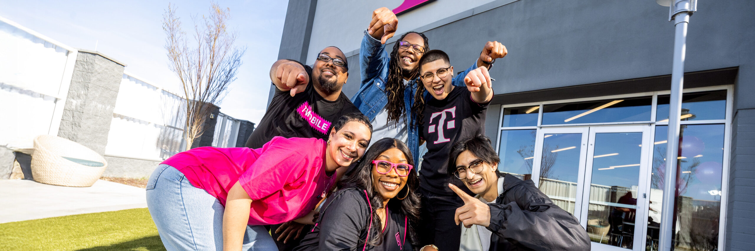 A group of T-Mobile employees posing and smiling outside of a T-Mobile office building.