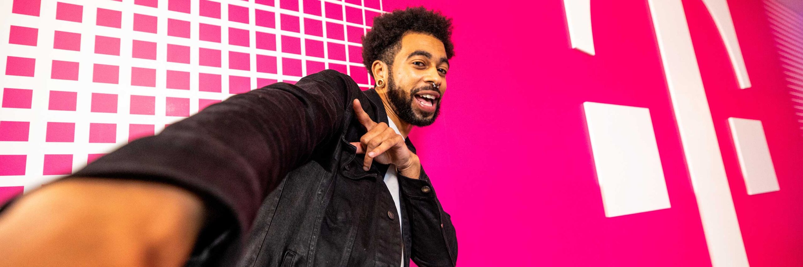 A T-Mobile employee taking a selfie in front of a bright pink T-Mobile branded wall.