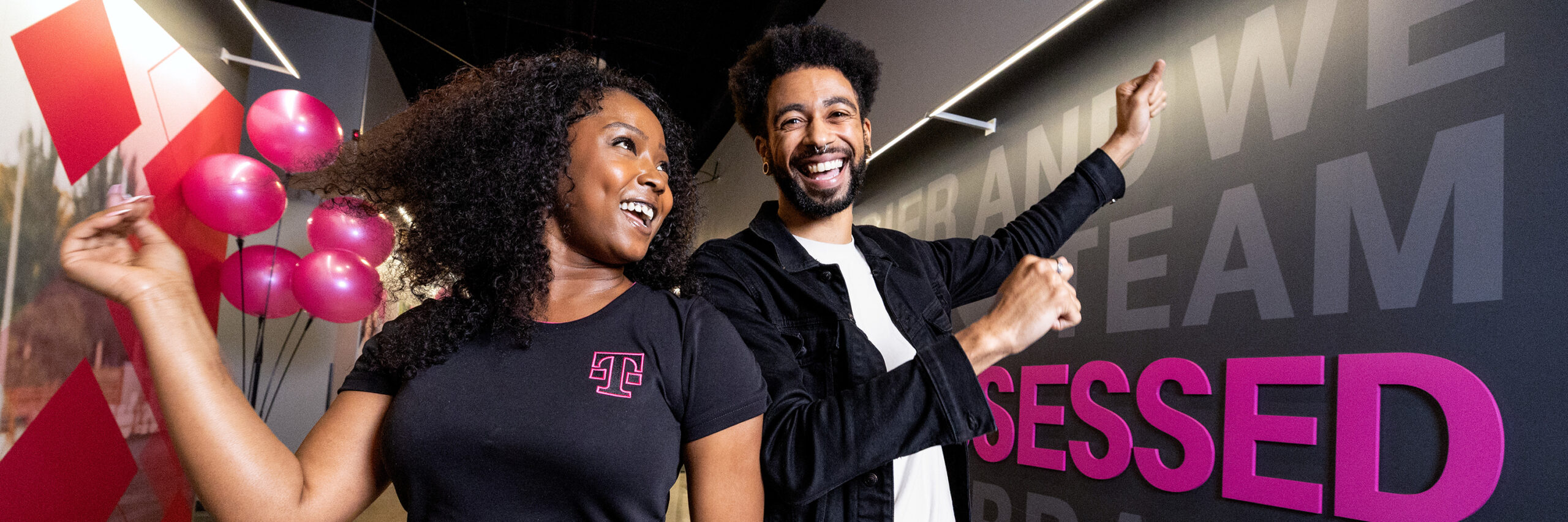 Two T-Mobile employees in a hallway with pink balloons and a gray wall.