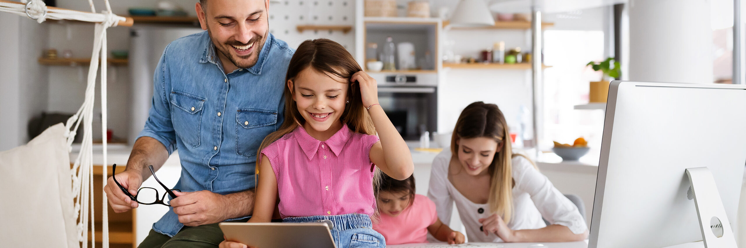 A family in a modern kitchen, with a child using a tablet at the table.