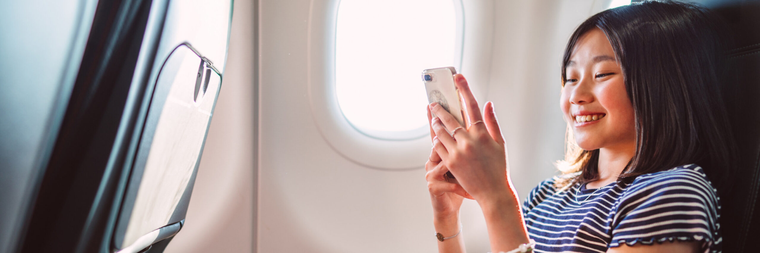 A teenager using a smartphone in an airplane seat by the window.